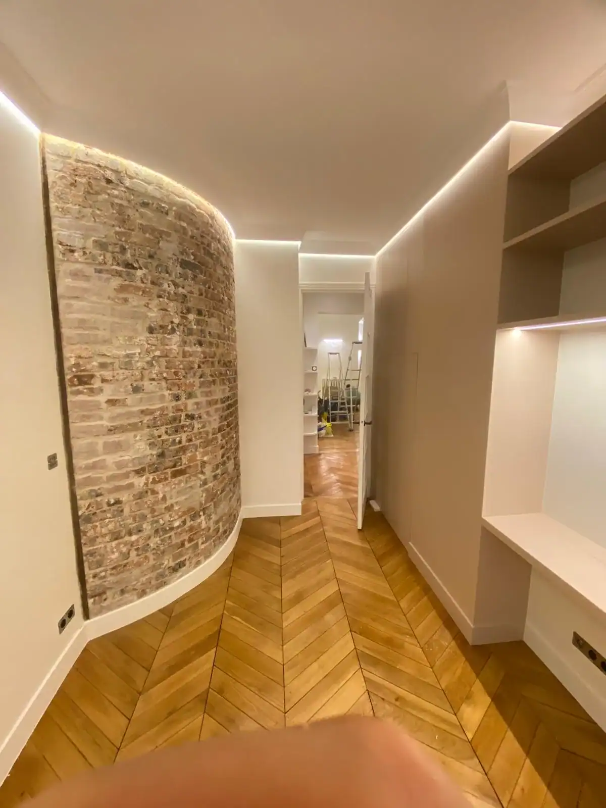 Couloir avec mur de brique courbe, parquet chevron et LED encastrée — Les Artistes