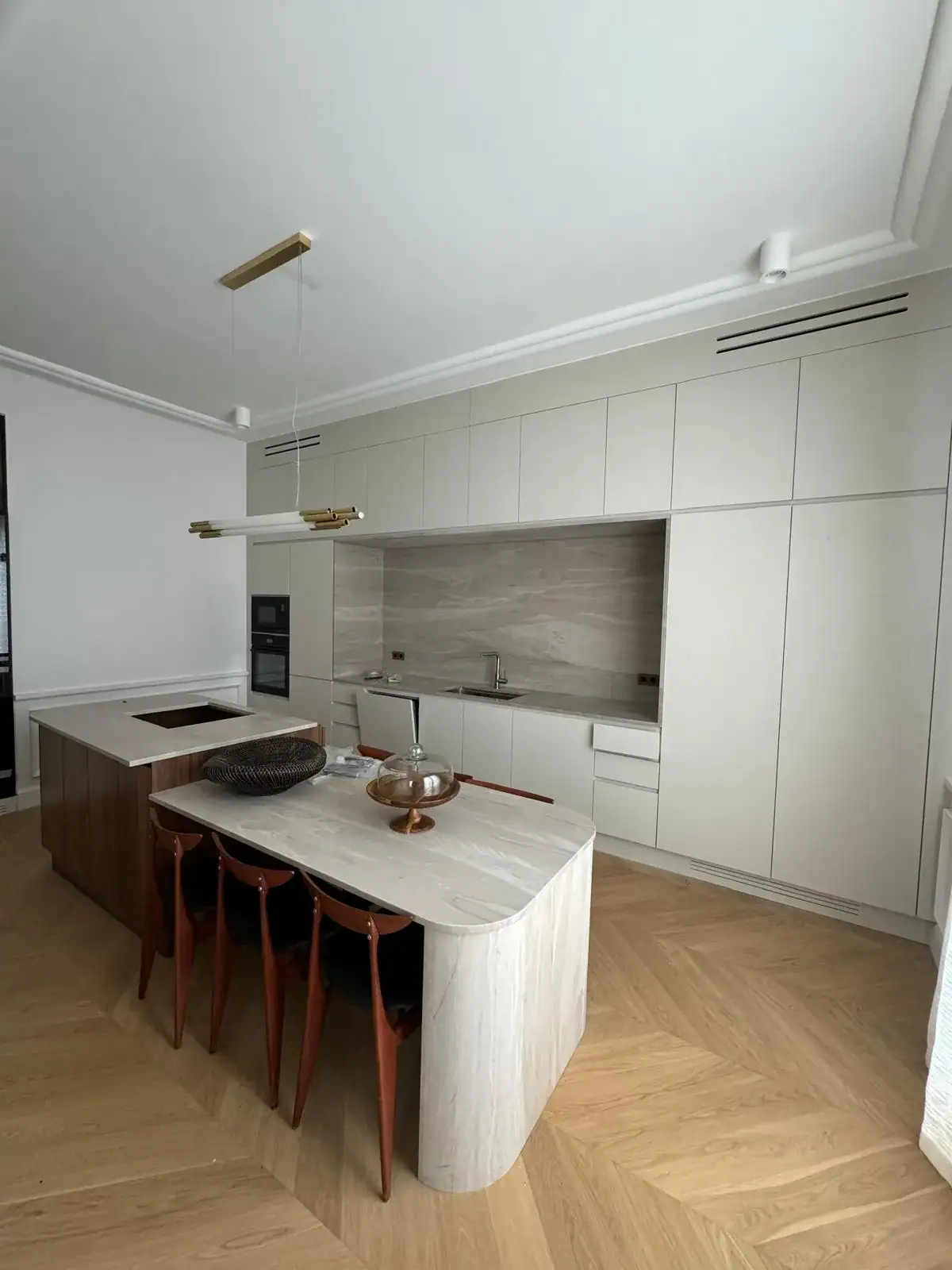Cuisine moderne sans poignées, îlot en pierre et parquet chevron — rénovation Les Artistes