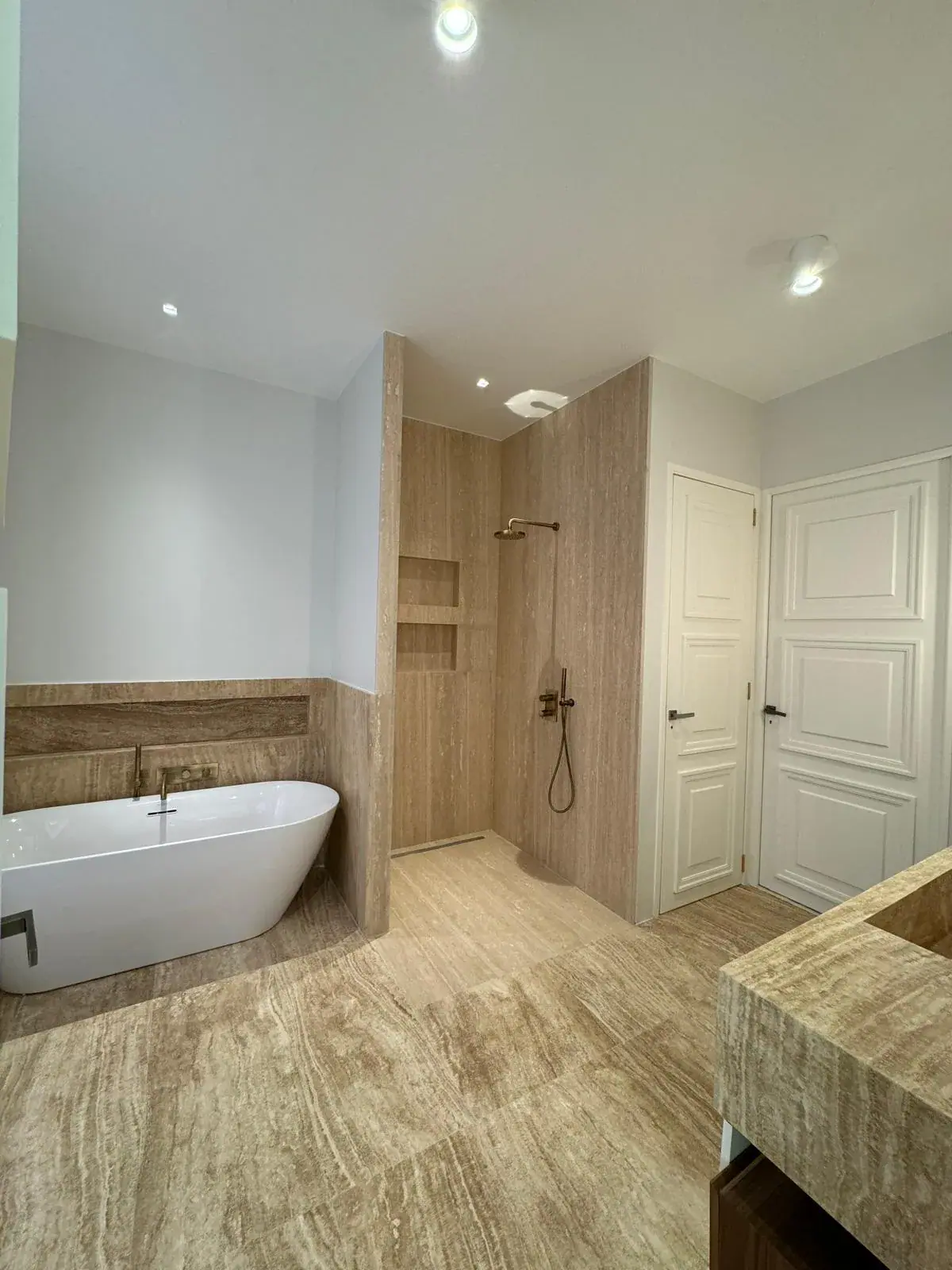 Salle de bain travertin avec baignoire îlot et douche walk-in robinetterie laiton — Les Artistes